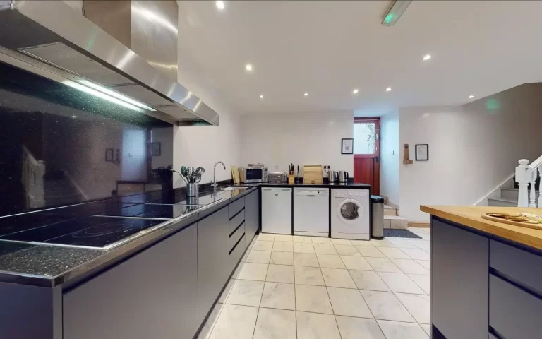 Modern fitted kitchen at Chels Barn, Toft Estate, featuring contemporary appliances and traditional wooden ceiling beams.