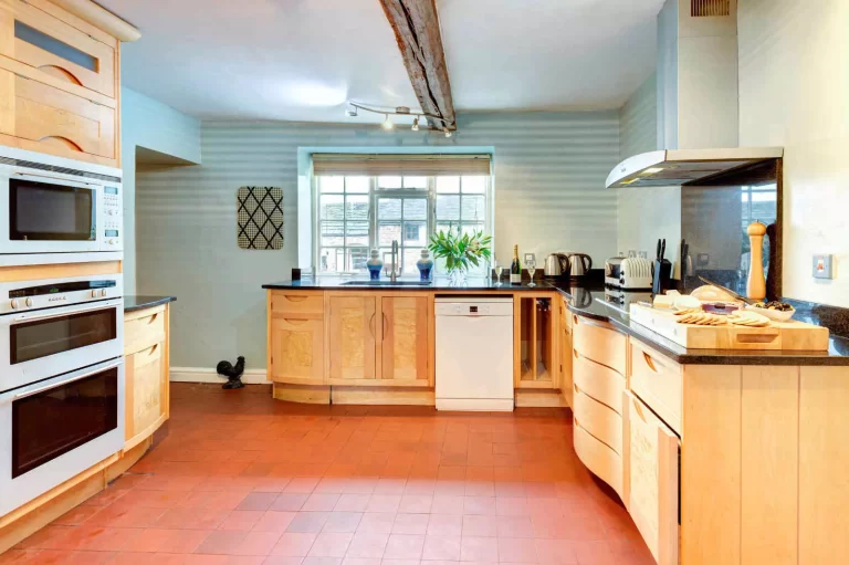 Rustic kitchen at Toft Hall, Toft Estate, featuring light wood cabinets, black worktops and terracotta tiled flooring.